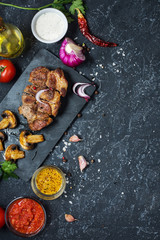 Juicy pork steak with spices and grilled mushroomson dark stone background. Top view