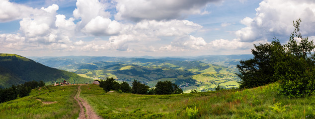 Fototapeta premium panorama of beautiful landscape in mountains. gorgeous view from Borzhava mountain ridge. road down the grassy hill to tourist base. wonderful summer weather with cloudy sky