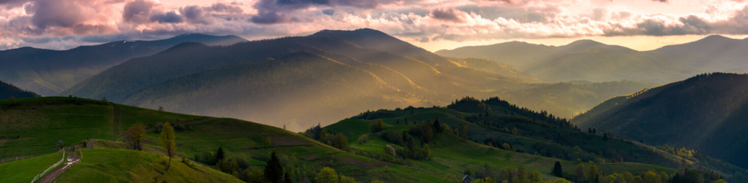 gorgeous panorama of countryside at sunset in springtime. landscape with rural fields on rolling hills and mountain ridge in sunlight in the distance