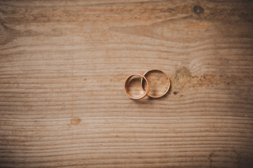 Two wedding rings of gold lie on a wooden surface, a view from the top.