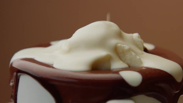 cup of hot chocolate with a cream and liquid white chocolate pouring on it. CLoseup of turning cup