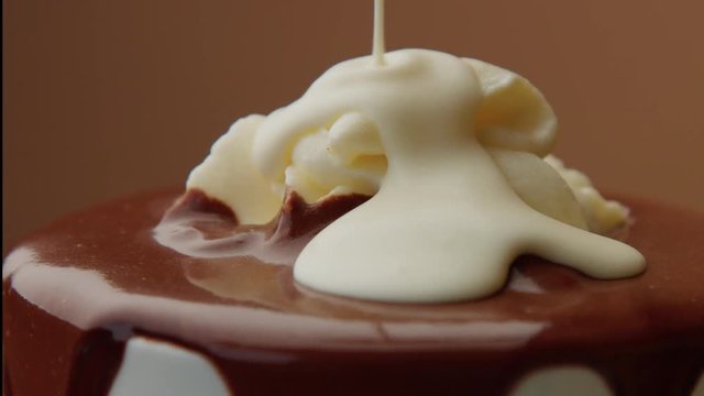 cup of hot chocolate with a cream and liquid white chocolate pouring on it. CLoseup of turning cup