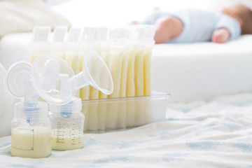 Breast milk frozen in storage bag and baby lying on background