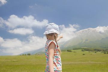 Little girl in Italian Apennines of Abruzzi region pointing at big mountain ridge view