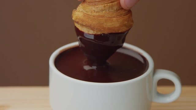 closeup of croissant immerse into hot chocolate in cup. Hot chocolate take out of cup making smuges