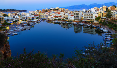 Beautiful southern town of Agios Nikolaos at summer evening. Boats swing on the water of the lake Voulismeni at the pier with evening lights. Crete Island. Greece