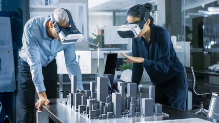 Male and Female Architects Wearing  Augmented Reality Headsets Work with 3D City Model. High Tech Office Professional People Use Virtual Reality Modeling Software Application.