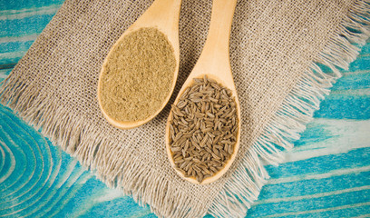 Fototapeta na wymiar Ground cumin in a spoon and whole cumin on the wooden background.