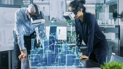 Male and Female Architects Wearing  Augmented Reality Headsets Work with 3D City Model. High Tech...