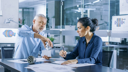 Experienced Male and Female Industrial Engineers have Discussion, Making Adjustment and Perfecting Parts, They Work on a Machinery Component Design. They Office is Stylish and Modern Looking.
