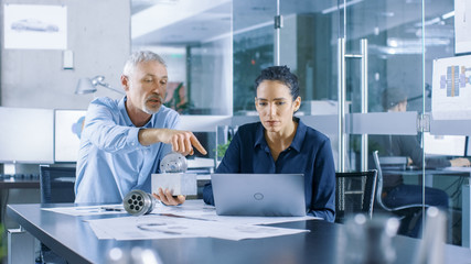 Experienced Male and Female Industrial Engineers have Discussion, Making Adjustment and Perfecting Parts, Type Corrections on a Laptop, They Work on a Machinery Component Design.