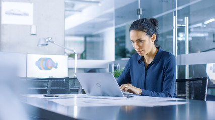 Beautiful Female Data Analyst sitting at the Table Works on a Laptop. Stylish Woman in the Modern...