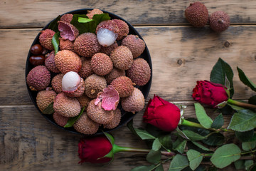 Still life of fresh lychee fruits in a black plate on a wooden background. Rustic style. Decorated with red roses