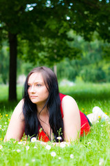 young woman with red dress and long hair lying on the meadow