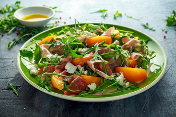 Fresh Peach salad with Parma ham, feta cheese and vegetables in a green plate. healthy food