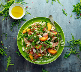 Fresh Peach salad with Parma ham, feta cheese and vegetables in a green plate. healthy food