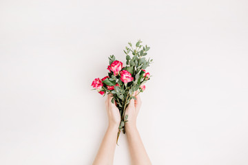 Woman hands hold rose flowers and eucalyptus branch bouquet. Flat lay, top view spring background.