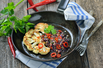 Veganes Gericht: Gebratener Blumenkohl mit pikanten roten Petersilien-Zwiebeln in der Pfanne serviert – Fried  slice of cauliflower topped with red parsley onions with red chili peppers 