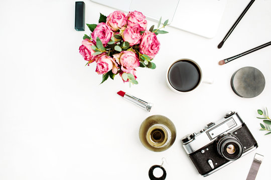 Feminine flat lay, top view workspace with rose flowers bouquet, vintage photo camera, coffee cup and accessories on white background. Women home office concept.