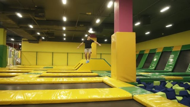 Young spotive athlete excellently trained jums over trampoline sections performing body twists.