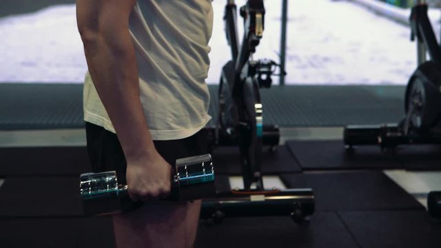Young guy doing exercises with dumbbells at biceps. Strength and motivation