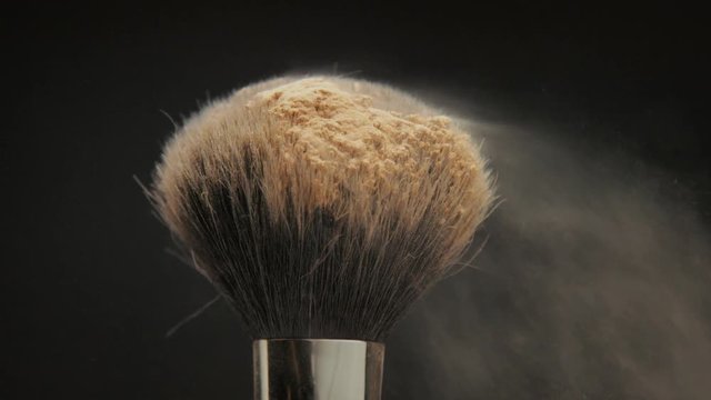 closeup of black brush with a facial powder on it and blowing out by wind