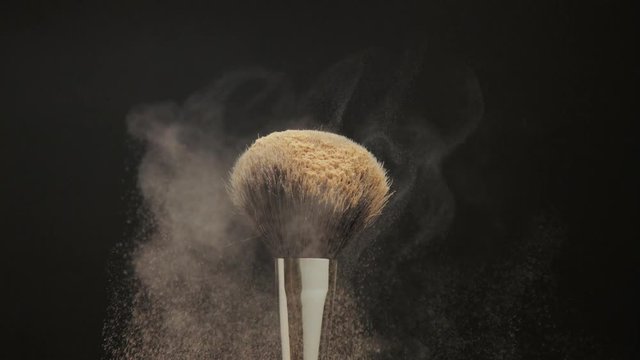 closeup of black brush with a facial powder on it and another brush falling on