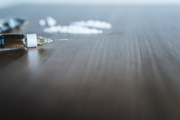 Heroin syringe with needle on a table with cocaine in the background.