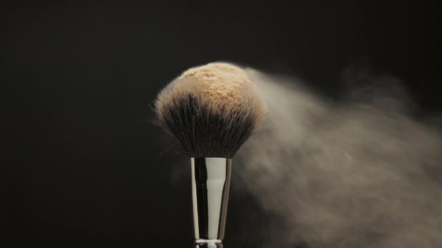 closeup of black brush with a facial powder on it and blowing out by wind