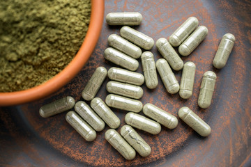 Close up Green capsules and powder on a clay brown plate on a burlap rustic background. Dietary...