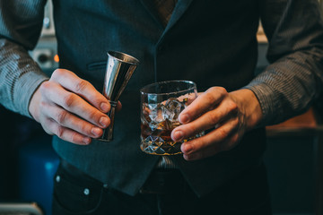 Bartender making alcoholic cocktail, metal jigger and bar environment
