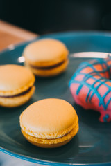 Tasty delicious yellow macaroons and donats on blue plate