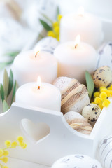 Fototapeta na wymiar Beautiful Easter composition with white lit candles in a white wooden box with decorated Easter eggs, olive branches and yellow mimosa flowers as a symbol of spring