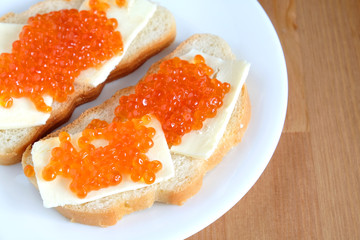 Two sandwiches with butter and red salmon caviar on white bread lies on white round plate on wooden background top view