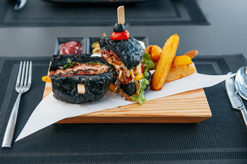 Black Burger - Charcoal Burger with fried onion lettuce tomato cut in half on wooden board