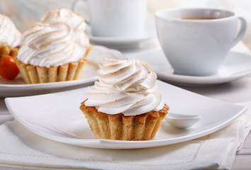 Delicious tartlets with meringue on top. Coffee and cupcakes served on white table.