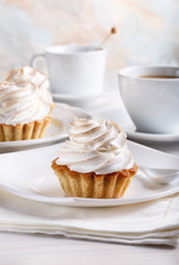 Delicious tartlets with meringue on top. Coffee and cupcakes served on white table.