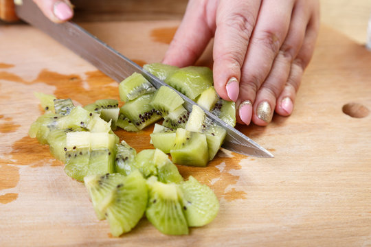 The woman cuts into small pieces a knife kiwi on a cutting board. Close-up, horizontal frame