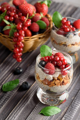 Two glasses of chia pudding with fresh strawberries, raspberries and blueberries. Basket with berries. On a wooden grey background.