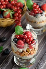 Two glasses of chia pudding with fresh strawberries, raspberries and blueberries. Basket with berries. On a wooden grey background.