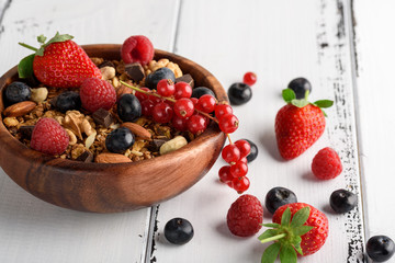 Bowl of homemade granola with yogurt and fresh berries on wooden background