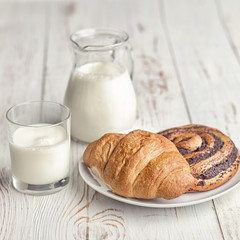 A jug of milk and an appetizing croissant on a village table in the morning ligh