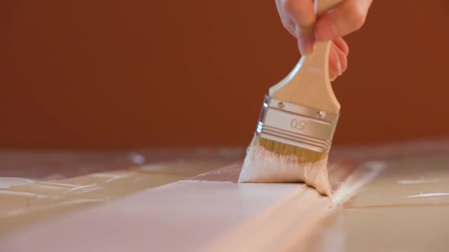 Close-up video of girl's hand with a brush painting wooden desk