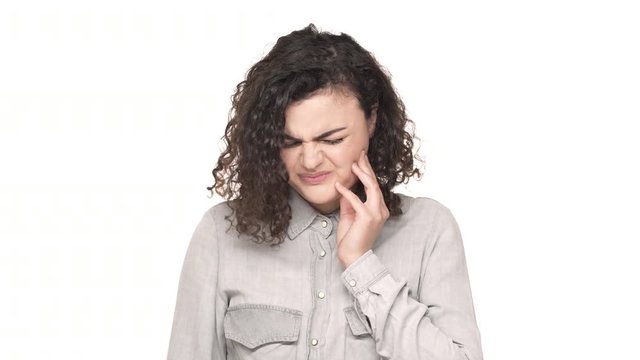 Portrait of upset woman with curly hair touching her cheek and suffering from toothache, isolated over white background. Concept of emotions