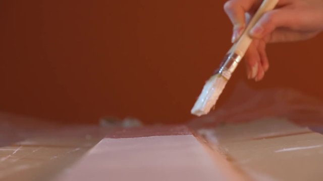 Close-up video of girl's hand with a brush painting wooden desk