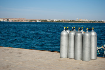 Naklejka premium Group eight cylinders with air. eight aluminum cylinders on sea dock. Empty oxygen tanks on pier. Blue ocean and white steel cylinders. Closeup of eight divers aluminum tanks on pier.