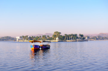 Colorful boats stationed on the famous lake fateh sagar in Udaipur floating on the beautiful blue water. The nehru park island and aravali hills are visible in the background.