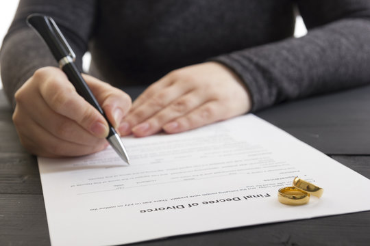 Hands of wife, husband signing decree of divorce, dissolution, canceling marriage, legal separation documents, filing divorce papers or premarital agreement prepared by lawyer. Wedding ring