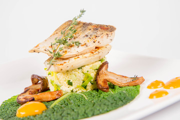 Fried zander, millet with green vegetables, fried boletus with thyme on a green leaf with some egg yolks on a white background