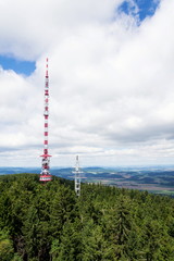Two telecommunication towers with transmitters and aerials in forest on sunny summer day on Mount...